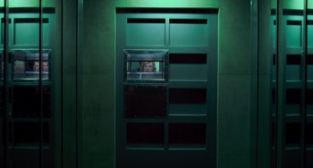 Movie still from “Resident Evil” (2002), directed by Paul W.S. Anderson – A person looking out of a window in a green room; Wide shot, Low angle