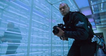 Movie still from “Resident Evil” (2002), directed by Paul W.S. Anderson – A man holding a gun while standing next to a wall; Medium shot, Low angle