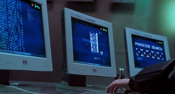 Movie still from “Resident Evil” (2002), directed by Paul W.S. Anderson – Two computer monitors are on a desk with a hand on a keyboard; Medium shot, Over the shoulder angle