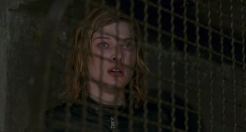 Movie still from “Resident Evil” (2002), directed by Paul W.S. Anderson – A woman with long hair looking through a fence; Close Up shot, Low angle