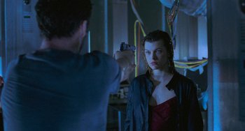 Movie still from “Resident Evil” (2002), directed by Paul W.S. Anderson – A man pointing a gun at a woman in front of a mirror; Medium shot, Over the shoulder angle