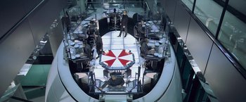Movie still from “Resident Evil: Afterlife” (2010), directed by Paul W.S. Anderson – A group of people sitting around a table with an umbrella on it; Wide shot, High angle