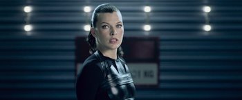 Movie still from “Resident Evil: Afterlife” (2010), directed by Paul W.S. Anderson – A woman in a black outfit standing next to a wall; Close Up shot, Low angle