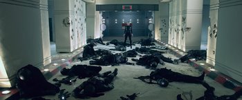 Movie still from “Resident Evil: Afterlife” (2010), directed by Paul W.S. Anderson – A man in a black suit standing in front of a group of dead bodies in a room; Wide shot, High angle