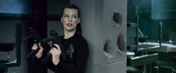 Movie still from “Resident Evil: Afterlife” (2010), directed by Paul W.S. Anderson – A woman holding a gun while standing next to a wall; Medium shot, Low angle