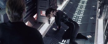 Movie still from “Resident Evil: Afterlife” (2010), directed by Paul W.S. Anderson – A woman in black shirt and black pants leaning on a wall; Medium shot, Overhead angle
