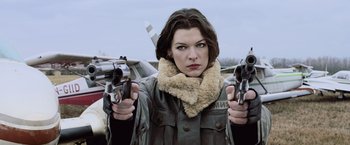 Movie still from “Resident Evil: Afterlife” (2010), directed by Paul W.S. Anderson – A woman in a shearling jacket holding two guns; Close Up shot, Low angle