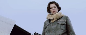 Movie still from “Resident Evil: Afterlife” (2010), directed by Paul W.S. Anderson – A woman with short hair wearing a coat and a fur collar; Medium shot, Low angle