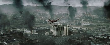Movie still from “Resident Evil: Afterlife” (2010), directed by Paul W.S. Anderson – An airplane flying over a large building in the middle of a city; Extreme Wide shot, High angle