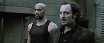 Movie still from “Resident Evil: Afterlife” (2010), directed by Paul W.S. Anderson – Two men standing next to each other in front of a building; Medium shot, Over the shoulder angle