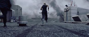Movie still from “Resident Evil: Afterlife” (2010), directed by Paul W.S. Anderson – A man is running through the air while holding a stick; Wide shot, High angle