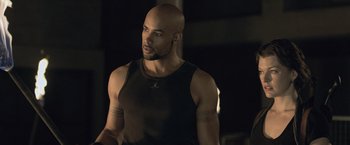 Movie still from “Resident Evil: Afterlife” (2010), directed by Paul W.S. Anderson – A bald man in a black tank top; Medium shot, Over the shoulder angle