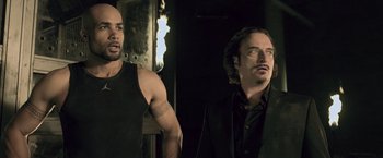 Movie still from “Resident Evil: Afterlife” (2010), directed by Paul W.S. Anderson – Two men standing next to each other in a dark room; Medium shot, Over the shoulder angle