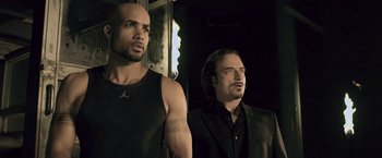 Movie still from “Resident Evil: Afterlife” (2010), directed by Paul W.S. Anderson – Two men standing next to each other in a dark room; Medium shot, Low angle