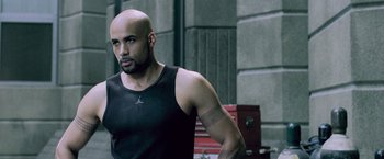 Movie still from “Resident Evil: Afterlife” (2010), directed by Paul W.S. Anderson – A bald man in a black tank top is looking at the camera; Close Up shot, High angle