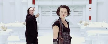 Movie still from “Resident Evil: Afterlife” (2010), directed by Paul W.S. Anderson – A man pointing a gun at a woman in a black outfit; Medium shot, Low angle