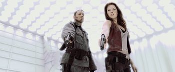Movie still from “Resident Evil: Afterlife” (2010), directed by Paul W.S. Anderson – A man and a woman are holding guns in their hands; Medium shot, Low angle