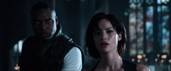 Movie still from “Resident Evil: Apocalypse” (2004), directed by Alexander Witt – A man and a woman standing next to each other in a dark room; Close Up shot, Over the shoulder angle