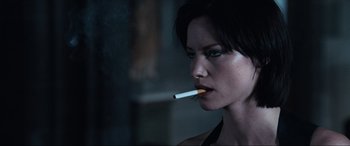 Movie still from “Resident Evil: Apocalypse” (2004), directed by Alexander Witt – A woman is smoking a cigarette in a dark room; Close Up shot, Over the shoulder angle
