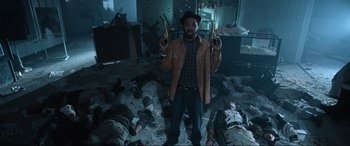 Movie still from “Resident Evil: Apocalypse” (2004), directed by Alexander Witt – A man standing in front of a group of corpses holding guns; Medium shot, Overhead angle