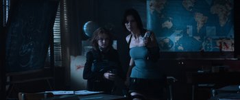 Movie still from “Resident Evil: Apocalypse” (2004), directed by Alexander Witt – A woman and a girl are standing in a dark room; Medium shot, Over the shoulder angle