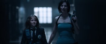 Movie still from “Resident Evil: Apocalypse” (2004), directed by Alexander Witt – A woman holding a gun next to a boy; Medium shot, Low angle