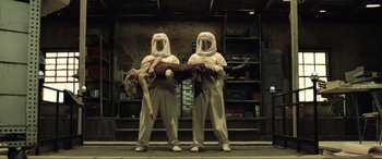 Movie still from “Resident Evil: Extinction” (2007), directed by Russell Mulcahy – A couple of people dressed in white holding a woman; Wide shot, Low angle