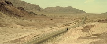 Movie still from “Resident Evil: Extinction” (2007), directed by Russell Mulcahy – A person riding a motorcycle down a road in the desert; Extreme Wide shot, High angle