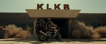 Movie still from “Resident Evil: Extinction” (2007), directed by Russell Mulcahy – A man riding a motorcycle in front of a building; Wide shot, Low angle