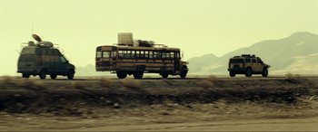 Movie still from “Resident Evil: Extinction” (2007), directed by Russell Mulcahy – An old school bus driving down a dirt road near mountains; Extreme Wide shot, Low angle
