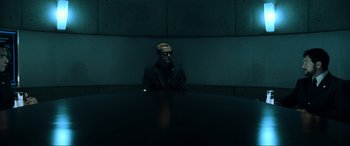 Movie still from “Resident Evil: Extinction” (2007), directed by Russell Mulcahy – A man sitting at a table in a dark room; Wide shot, Low angle