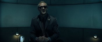 Movie still from “Resident Evil: Extinction” (2007), directed by Russell Mulcahy – A man in a suit and tie sitting in a dark room; Medium shot, Low angle