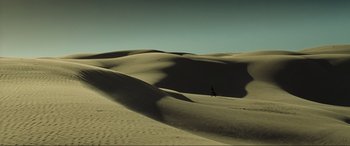 Movie still from “Resident Evil: Extinction” (2007), directed by Russell Mulcahy – A person is walking in the sand on a beach; Extreme Wide shot, High angle