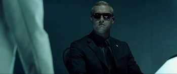 Movie still from “Resident Evil: Extinction” (2007), directed by Russell Mulcahy – A man in a suit and sunglasses sitting in a chair; Close Up shot, Low angle