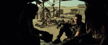 Movie still from “Resident Evil: Extinction” (2007), directed by Russell Mulcahy – A group of men sitting on top of a sandy beach; Wide shot, Over the shoulder angle