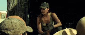 Movie still from “Resident Evil: Extinction” (2007), directed by Russell Mulcahy – A woman sitting on the ground wearing a baseball cap; Medium shot, Over the shoulder angle
