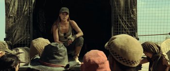 Movie still from “Resident Evil: Extinction” (2007), directed by Russell Mulcahy – A woman sitting on the ground wearing a hat; Medium shot, Over the shoulder angle