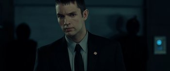 Movie still from “Resident Evil: Extinction” (2007), directed by Russell Mulcahy – A man in a suit and tie with a cross on his lapel; Close Up shot, Low angle