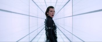 Movie still from “Resident Evil: Retribution” (2012), directed by Paul W.S. Anderson – Milla jovovich in a black outfit in front of a white wall; Medium shot, Low angle