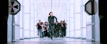 Movie still from “Resident Evil: Retribution” (2012), directed by Paul W.S. Anderson – A group of people in a room with a woman in a black costume; Wide shot, Low angle