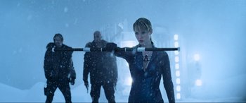 Movie still from “Resident Evil: Retribution” (2012), directed by Paul W.S. Anderson – A woman holding a barbell while standing in the snow; Medium shot, Over the shoulder angle