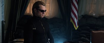 Movie still from “Resident Evil: Retribution” (2012), directed by Paul W.S. Anderson – A man wearing sunglasses and a black jacket; Medium shot, Over the shoulder angle
