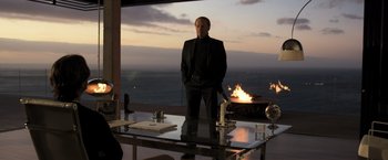 Movie still from “Resident Evil: The Final Chapter” (2016), directed by Paul W.S. Anderson – A man standing in front of a fire pit on top of a glass table; Wide shot, Over the shoulder angle