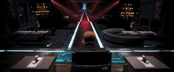 Movie still from “Resident Evil: The Final Chapter” (2016), directed by Paul W.S. Anderson – A man sitting in front of a stage with lights on it; Wide shot, Over the shoulder angle