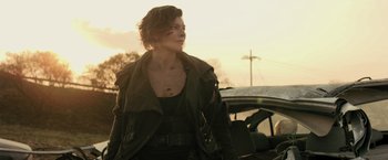 Movie still from “Resident Evil: The Final Chapter” (2016), directed by Paul W.S. Anderson – A woman in a leather jacket standing in front of a car; Medium shot, Low angle