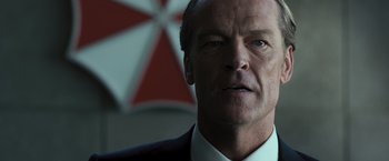 Movie still from “Resident Evil: The Final Chapter” (2016), directed by Paul W.S. Anderson – A man in a suit and tie in front of an umbrella; Close Up shot, Over the shoulder angle