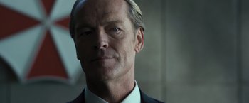 Movie still from “Resident Evil: The Final Chapter” (2016), directed by Paul W.S. Anderson – A man in a suit and white shirt looking at the camera; Close Up shot, Low angle