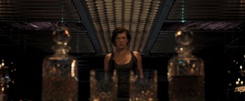 Movie still from “Resident Evil: The Final Chapter” (2016), directed by Paul W.S. Anderson – A woman standing in front of a table with glasses on top of it; Medium shot, Low angle
