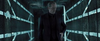 Movie still from “Resident Evil: The Final Chapter” (2016), directed by Paul W.S. Anderson – A man in a black suit standing next to a wall; Medium shot, Low angle