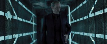 Movie still from “Resident Evil: The Final Chapter” (2016), directed by Paul W.S. Anderson – A man in a black suit standing in a dark room; Medium shot, Low angle